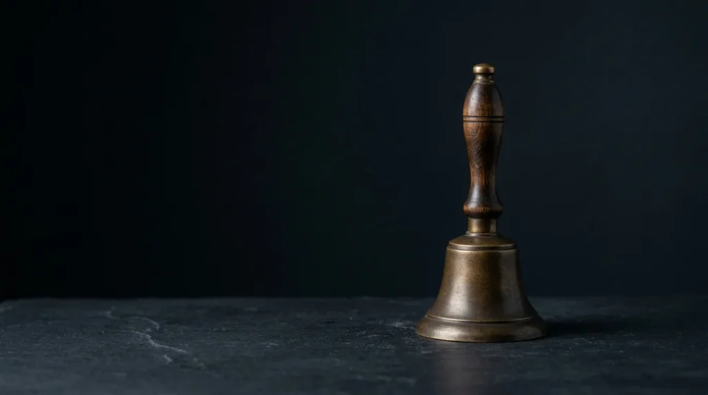 A small cast bronze hand bell with a dark turned wooden handle, resting on dark slate